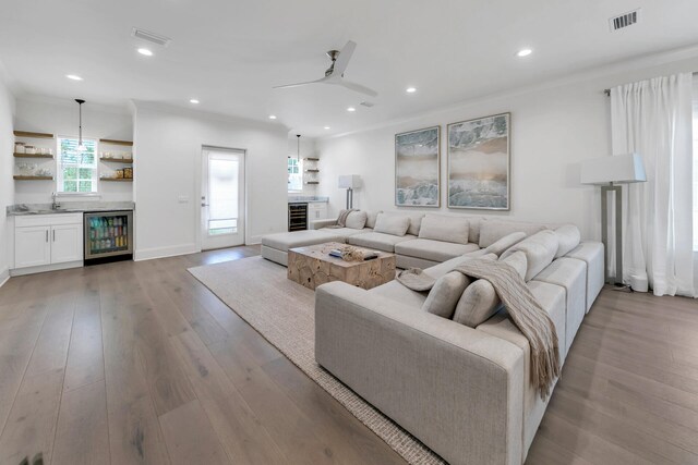 living room featuring ornamental molding, sink, wine cooler, light wood-type flooring, and ceiling fan