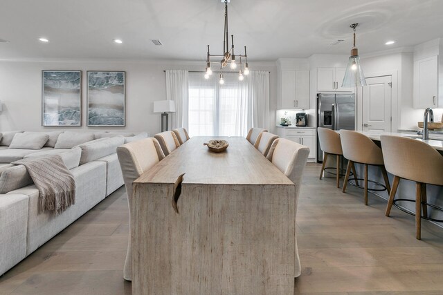 dining room featuring sink, light hardwood / wood-style floors, ornamental molding, and an inviting chandelier