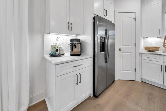 kitchen featuring light hardwood / wood-style floors, stainless steel fridge with ice dispenser, light stone countertops, and white cabinetry