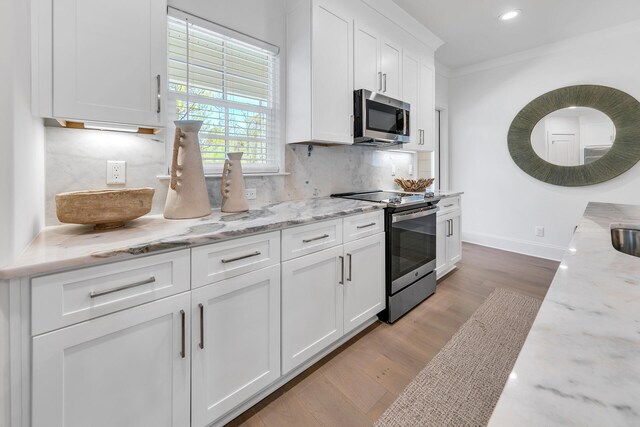 kitchen featuring ornamental molding, appliances with stainless steel finishes, light stone counters, light hardwood / wood-style floors, and tasteful backsplash