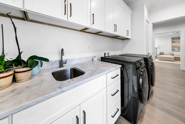 laundry area with light hardwood / wood-style floors, washer and dryer, sink, and cabinets