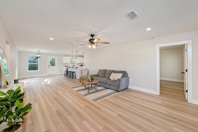 living room featuring ceiling fan with notable chandelier, a textured ceiling, and light hardwood / wood-style flooring