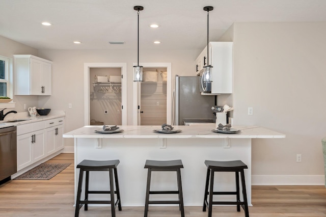 kitchen with appliances with stainless steel finishes, pendant lighting, light stone counters, white cabinets, and light hardwood / wood-style flooring