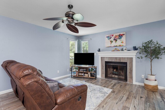 living room featuring a ceiling fan, a fireplace, baseboards, and wood finished floors