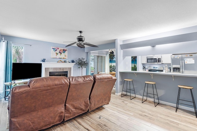 living area featuring a ceiling fan, light wood-type flooring, baseboards, and a tiled fireplace