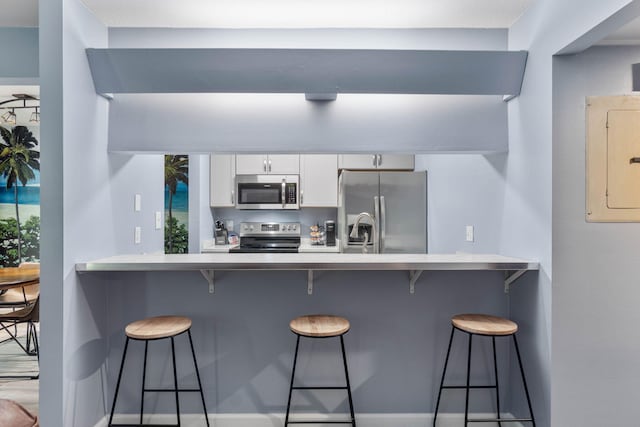 kitchen featuring light countertops, appliances with stainless steel finishes, a kitchen bar, and white cabinets