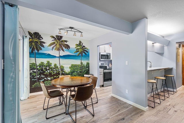 dining space featuring a textured ceiling, track lighting, light wood-type flooring, and baseboards