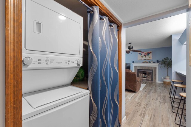 laundry area with stacked washer and dryer, laundry area, a ceiling fan, a glass covered fireplace, and light wood-style floors