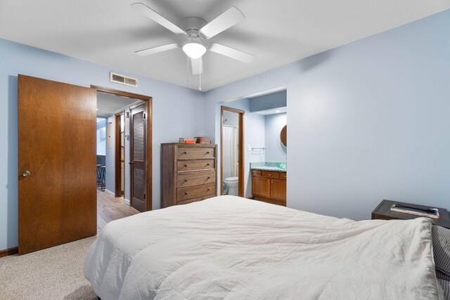 bedroom with a closet, visible vents, light carpet, ceiling fan, and ensuite bath