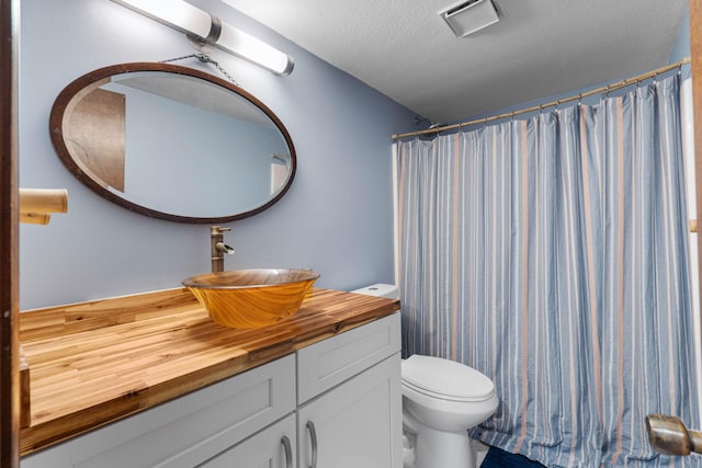 bathroom featuring visible vents, a shower with shower curtain, toilet, a textured ceiling, and vanity