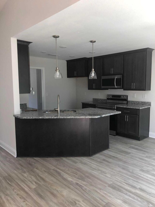 kitchen featuring light wood-type flooring, electric stove, hanging light fixtures, light stone counters, and sink