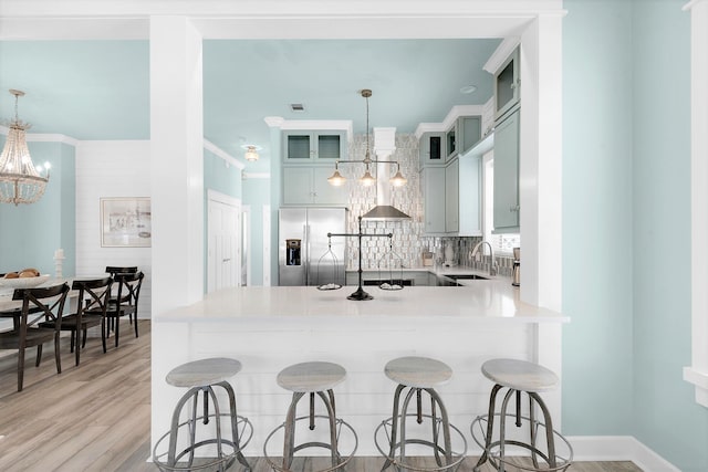 kitchen with light wood-type flooring, tasteful backsplash, hanging light fixtures, stainless steel fridge with ice dispenser, and an inviting chandelier