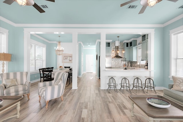 living room with light hardwood / wood-style flooring, ceiling fan with notable chandelier, and a healthy amount of sunlight