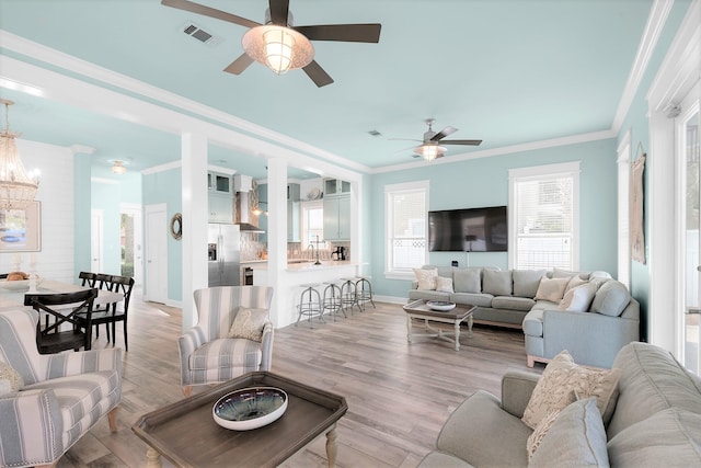 living room with sink, light wood-type flooring, crown molding, and ceiling fan with notable chandelier