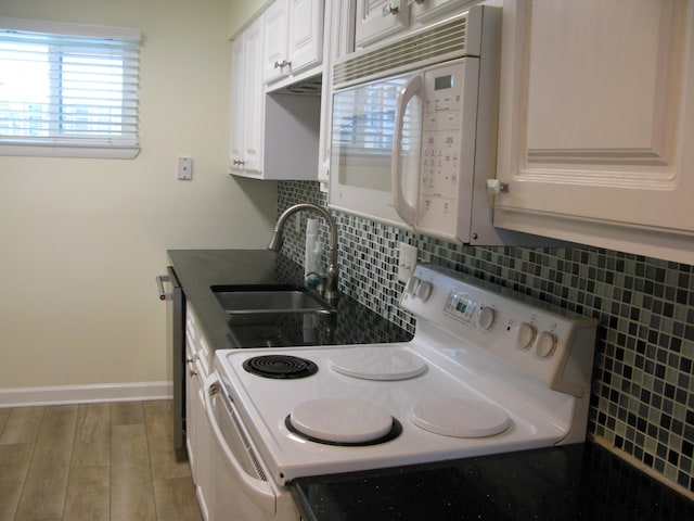 kitchen featuring dark countertops, backsplash, white cabinetry, a sink, and white appliances