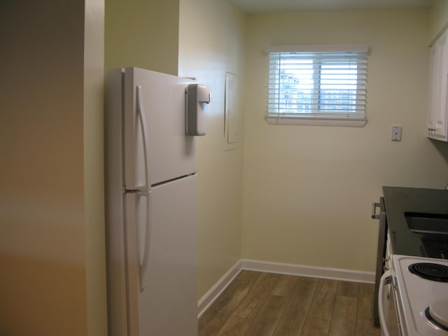 kitchen featuring white appliances, dark wood-style flooring, a sink, baseboards, and white cabinets