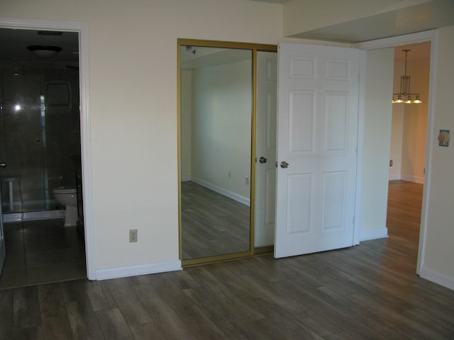 unfurnished bedroom featuring ensuite bath, a closet, baseboards, and dark wood-type flooring