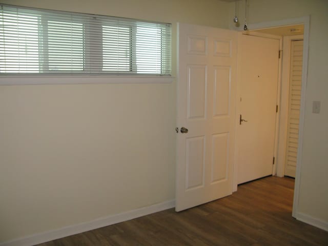 spare room with baseboards and dark wood-type flooring