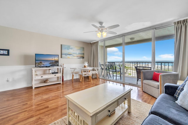 living room with light hardwood / wood-style floors, expansive windows, ceiling fan, and a water view