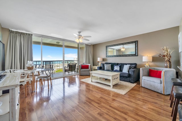 living room featuring ceiling fan, light hardwood / wood-style floors, and a wall of windows