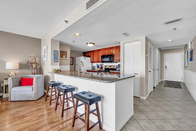 kitchen with dark stone counters, white refrigerator, light hardwood / wood-style flooring, stainless steel electric range, and kitchen peninsula