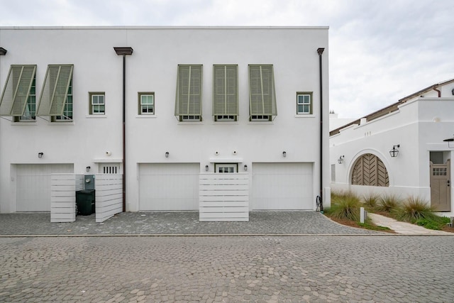 townhome / multi-family property with an attached garage, decorative driveway, and stucco siding