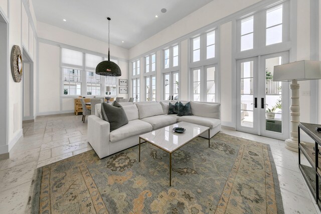 living room with french doors, plenty of natural light, a towering ceiling, and baseboards