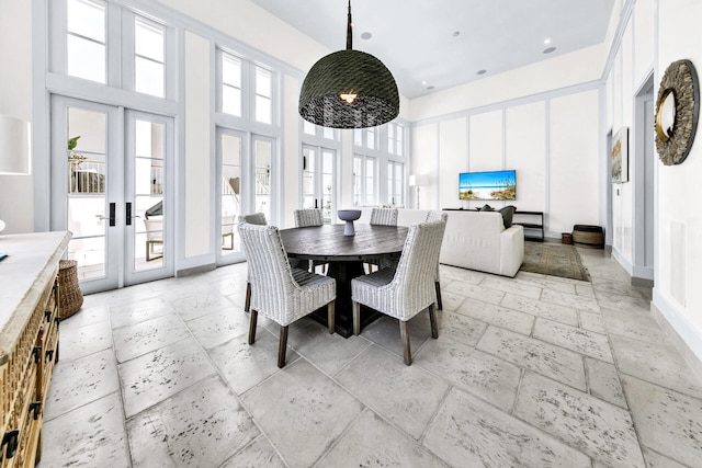 dining space with a high ceiling, baseboards, stone tile flooring, and french doors