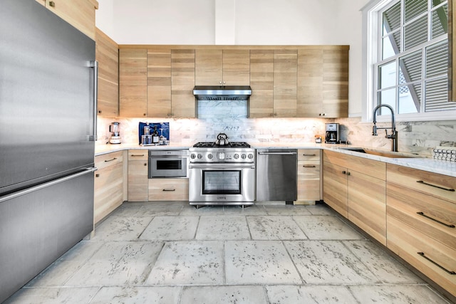 kitchen with premium appliances, under cabinet range hood, a sink, light countertops, and decorative backsplash