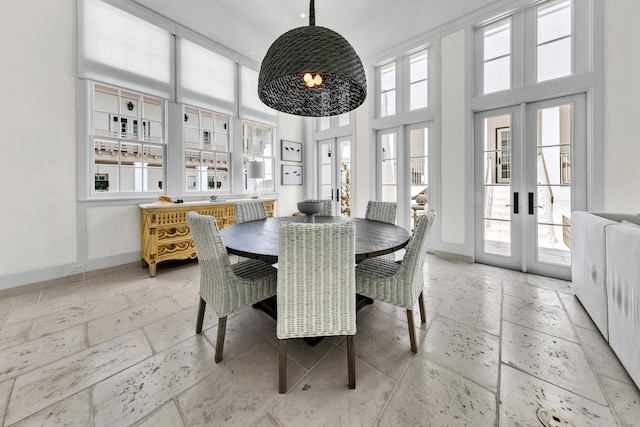 dining space featuring french doors, stone tile floors, a towering ceiling, and baseboards