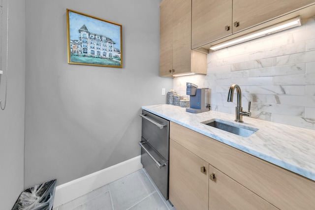 kitchen with tasteful backsplash, baseboards, light stone counters, light brown cabinets, and a sink