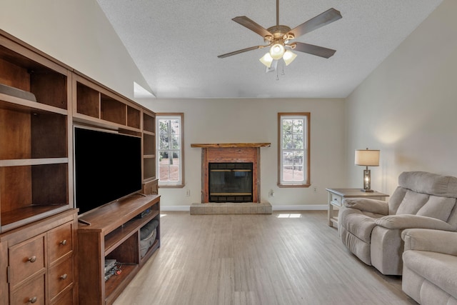 living room with a tile fireplace, vaulted ceiling, light hardwood / wood-style flooring, ceiling fan, and a textured ceiling