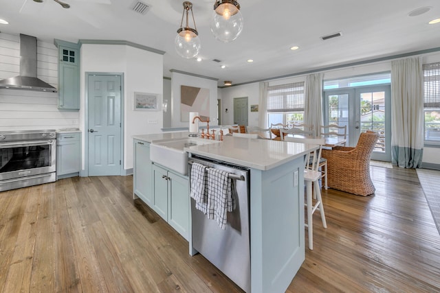 kitchen featuring wall chimney range hood, pendant lighting, stainless steel appliances, and an island with sink