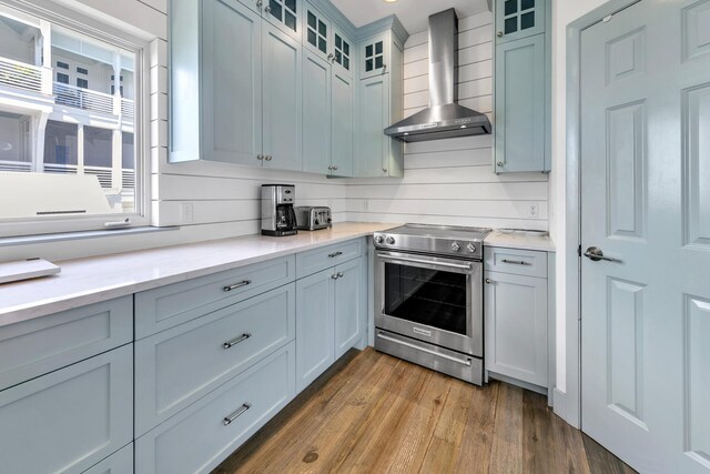 kitchen with light wood-type flooring, stainless steel electric stove, decorative backsplash, and wall chimney range hood