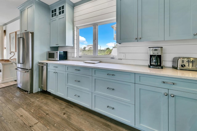 kitchen with dark wood-type flooring, appliances with stainless steel finishes, and wooden walls