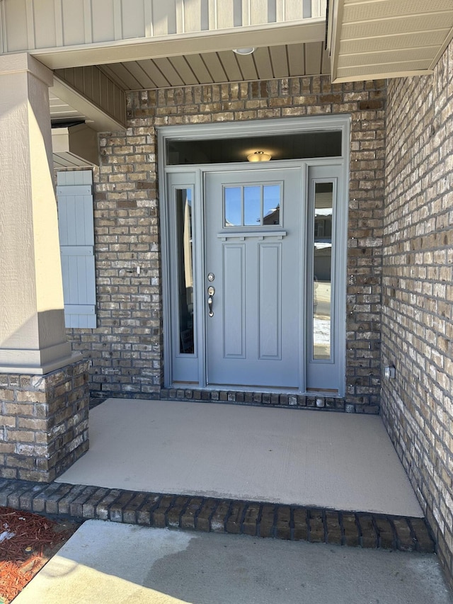 entrance to property with board and batten siding, brick siding, and a patio