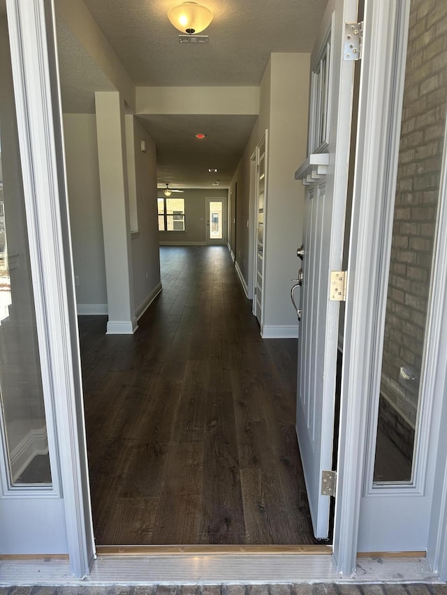 corridor with dark wood-style flooring, visible vents, and baseboards