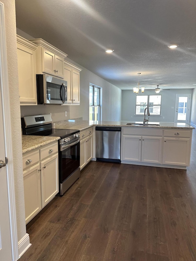 kitchen with dark wood-type flooring, sink, appliances with stainless steel finishes, kitchen peninsula, and light stone countertops