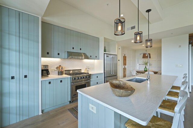 kitchen featuring a kitchen breakfast bar, decorative backsplash, high end appliances, and wall chimney range hood