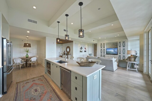 kitchen featuring appliances with stainless steel finishes, sink, light wood-type flooring, a kitchen island with sink, and hanging light fixtures