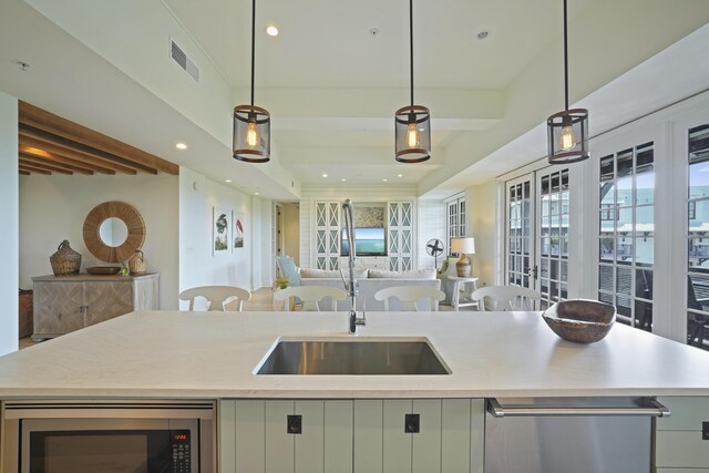 kitchen featuring pendant lighting, stainless steel microwave, sink, beamed ceiling, and a center island with sink