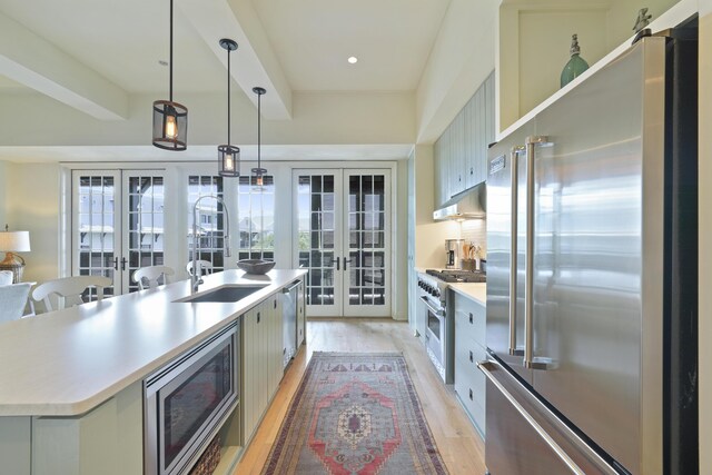 kitchen featuring wall chimney range hood, built in appliances, light hardwood / wood-style flooring, pendant lighting, and french doors