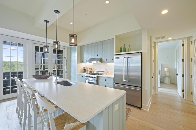 kitchen with a breakfast bar, backsplash, light wood-type flooring, an island with sink, and high quality appliances