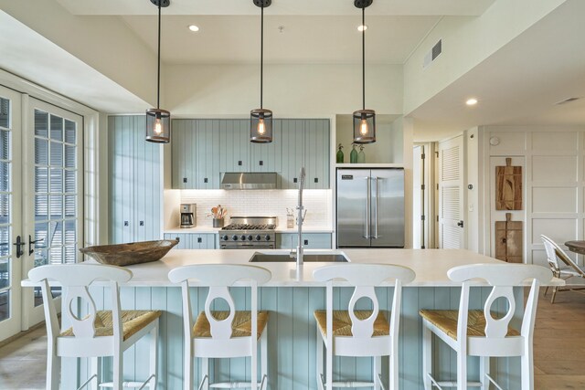 kitchen with light wood-type flooring, tasteful backsplash, a breakfast bar, a center island with sink, and high quality appliances