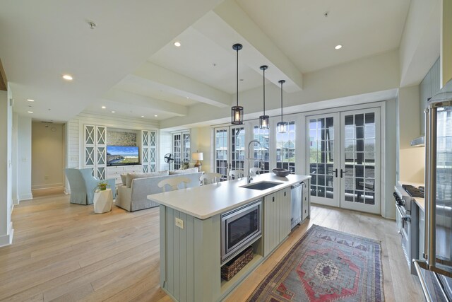 kitchen with an island with sink, french doors, light hardwood / wood-style floors, decorative light fixtures, and stainless steel appliances