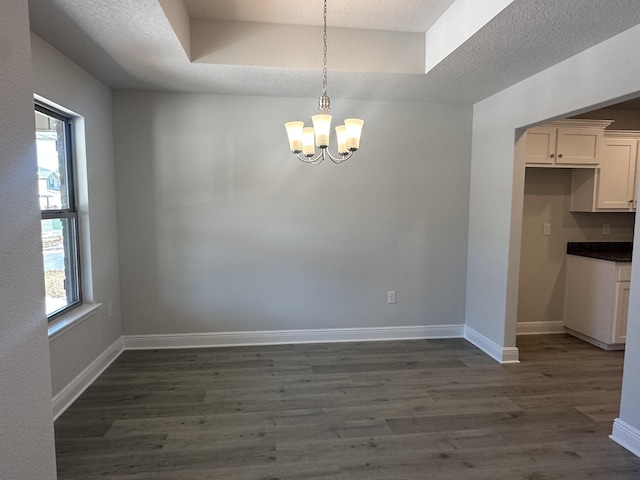 unfurnished dining area featuring a chandelier, a raised ceiling, dark wood-style floors, and baseboards