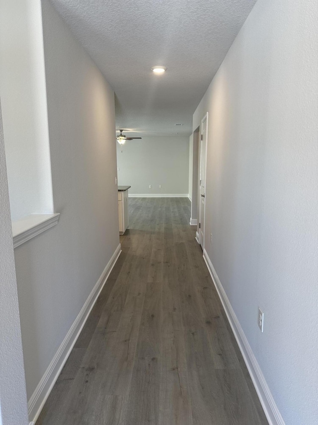 hallway with a textured ceiling, baseboards, and dark wood-style flooring