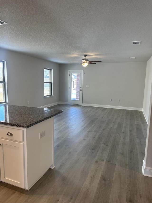 kitchen with open floor plan, white cabinetry, dark stone countertops, wood finished floors, and baseboards