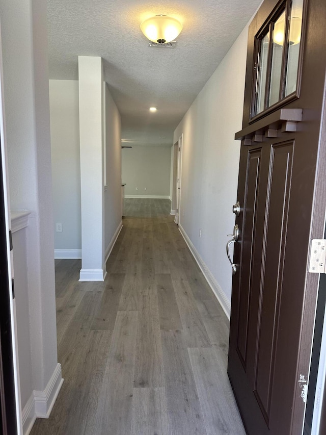 hall featuring light wood-style flooring, baseboards, and a textured ceiling