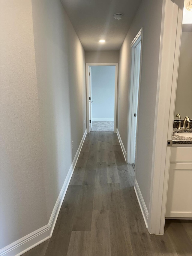 hallway featuring a sink, dark wood finished floors, and baseboards